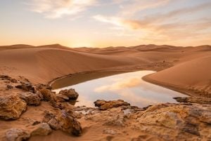 Still pool of water among sand dunes and mineral-rich rocks at golden hour